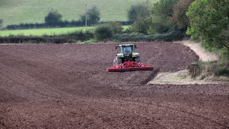 A-farmer-driving-a-tractor-tilling-and-raking-a-ploughed-field-during-autumn-in-the-Worcestershire-Countryside,-England