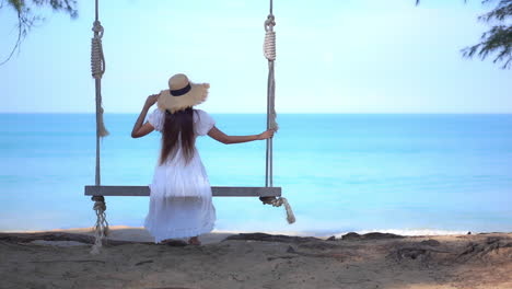Einsame-Frau-Auf-Schaukel-Am-Tropischen-Strand-In-Sommerkleid-Und-Hut,-Atemberaubender-Blick-Auf-Das-Blaue-Meer-Und-Den-Horizont,-Vollbild