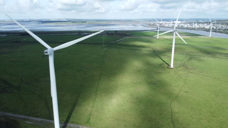 Aerial-view-flying-around-renewable-energy-wind-farm-wind-turbines-spinning-on-British-countryside-rear-orbit-right