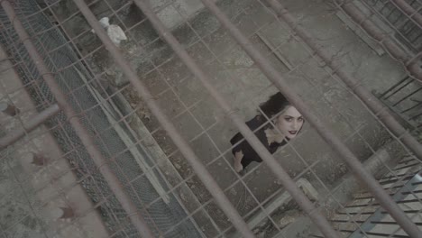 A-gothic-girl-in-black-clothes-with-a-scary-smile-stretches-her-arms-up-from-the-cage-in-which-she-is-trapped