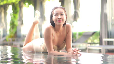 Mujer-Asiática-Sexy-En-Traje-De-Baño-Tumbada-En-El-Borde-De-La-Piscina-Infinita-Y-Disfrutando-En-El-Día-Del-Spa,-Fotograma-Completo