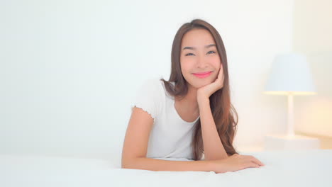 Portrait-of-Young-Beautiful-Satisfied-Asian-Woman-on-Bed-Smiling-to-Camera,-Full-Frame