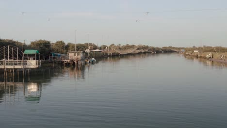 Fishermen-huts-with-fishing-nets-and-fishing-equipment-on-the-river-at-morning,Lido-di-Dante,-Fiumi-Uniti,-Ravenna-near-Comacchio-valley