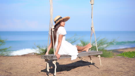 Exotic-Woman-in-White-Summer-Dress-on-Wooden-Swing-by-Tropical-Beach-on-Sunny-Day,-Full-Frame