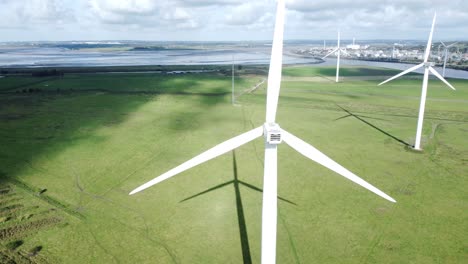Aerial-view-flying-around-renewable-energy-wind-farm-wind-turbines-spinning-on-British-countryside-slow-orbit-left-shot
