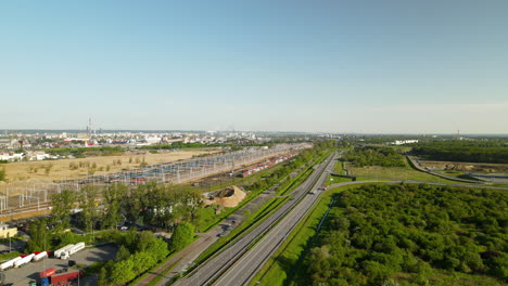 Aerial-flight-showing-driving-cars-on-highway-beside-train-station-and-Gdansk-City-in-background,Poland