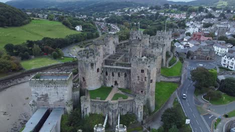 Medieval-Conwy-castle-walled-market-town-aerial-view-descending-countryside-shot