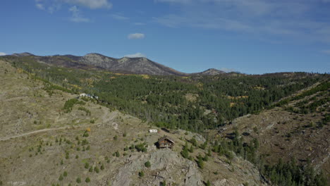 Aerial-moving-past-small-remote-cabin-on-mountainside-outcropping,-4K