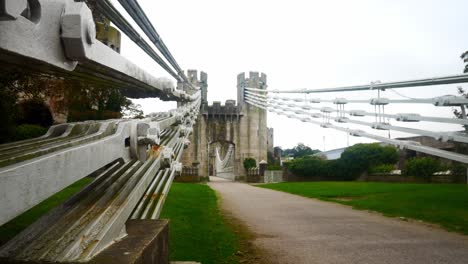 Conwy-castle-huge-steel-engineering-bridge-cables-low-angle-along-pathway-dolly-left