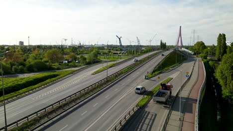 Luftaufnahme-Von-Fahrzeugen,-Die-Auf-Der-Straße-Mit-Hafenkränen-Auf-Dem-Hafen-Von-Danzig-Im-Hintergrund-In-Polen-Fahren