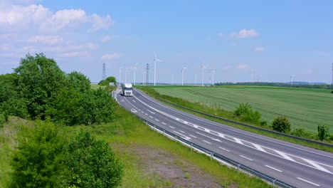 White-Truck-driving-on-a-country-road-with-huge-ecological-Wind-Farm-in-background