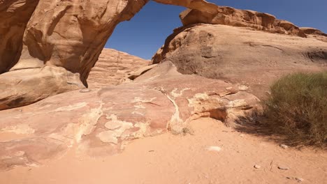 Wadi-Rum,-Jordan,-Low-Angle-View-of-Natural-Sandstone-Arch-on-Hot-Sunny-Day,-Tilt-Up