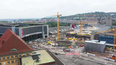 Aerial-of-construction-site-of-main-train-station-Stuttgart-S21-with-cranes-and-construction-workers-descending-over-Stuttgart,-Germany