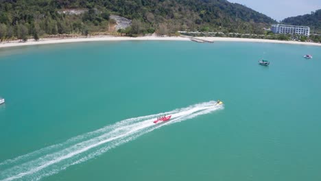 Aerial-footage-following-Banana-boat-full-of-people-having-fun-and-cruising-in-high-speed-attached-on-powerboat,-watersport