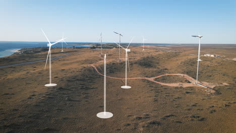 Aerial-view-showing-wind-turbine-farm-with-digital-holograms-printing-modern-renewable-windmills---Beautiful-sunny-day-with-blue-sky-and-ocean-in-background---Future-concept-of-agricultural-field