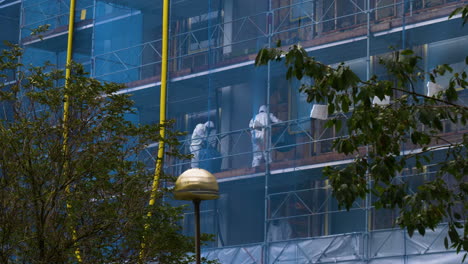 Asbestos-abatement-team-Working-on-building,-trees-waving-in-foreground