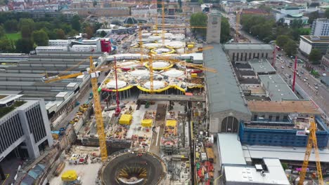 Drone-flying-over-huge-construction-site-of-main-train-station-Stuttgart-S21-with-cranes-and-construction-workers-in-Stuttgart,-Germany