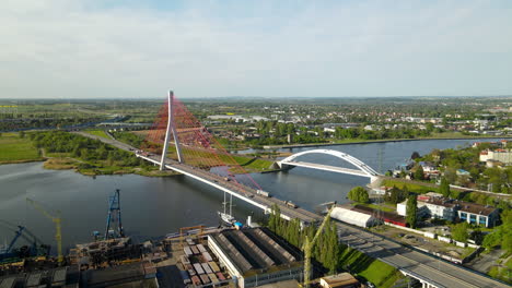 Aerial-View-Third-Millennium-John-Paul-II-bridge-which-links-the-Northern-Port-of-Gdansk-with-the-national-road-network,-port-cargo-terminal-in-foreground,-And-Railway-Bridge-Over-Martwa-Wisla-River
