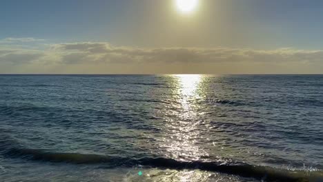 Slow-tilt-up-from-the-gentle-lapping-waves-of-a-deserted-tropical-beach-at-sunset-towards-the-clear-horizon-as-the-sun-descends-and-the-sky-turns-yellow