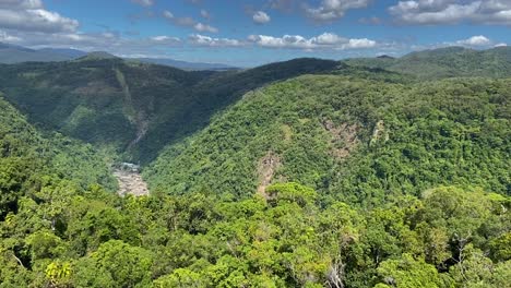 High-aerial-view-over-rocky-escarpments,-overlooking-a-deep-valley-to-reveal-the-stunning-vista-of-the-dense-tropical-rain-forest-shrouded-mountains-of-North-Queensland