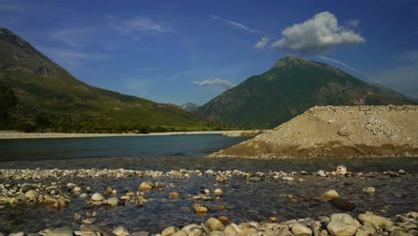 River-landscape-with-clean-water-streaming-on-pebbles-and-mountains-background,-Vjosa-Albania