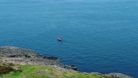 Small-fishing-boat-sailing-colourful-blue-ocean-water-view-from-Welsh-hillside-slope
