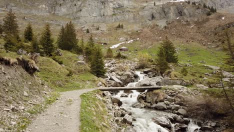 Hiking-trail-crossing-river-via-little-bridge-in-the-Swiss-Alps