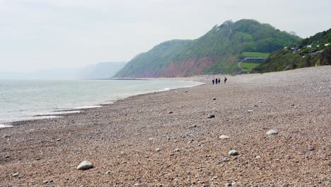 Distant-walkers-enjoy-the-scenery-of-the-pebble-beach-at-Branscombe-in-Devon-on-the-English-Channel-coast