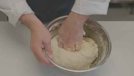 A-baker-skillfully-kneads-dough-in-a-large-metal-bowl