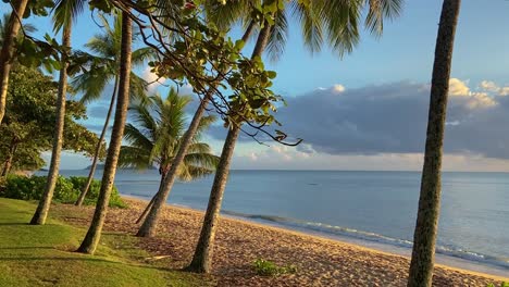 Beautiful,-quiet-tropical-beach-at-sunrise-sunset-looking-towards-Double-Island-Point,-with-gently-lapping-waves-under-a-blue-and-gold-tinged-sky-with-palm-fringed-shoreline-of-north-Queensland