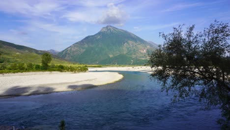 River-is-flowing-pebbles-banks,-beautiful-landscape-with-mountain-background-in-Vjosa