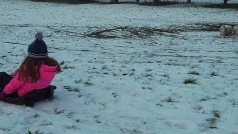 Young-girl-in-sled-pulled-by-parent-on-snowy-field-slomo