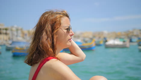 Red-haired-girl-in-profile-admiring-the-beauty-of-the-fishing-village-of-Marsaxlokk-in-Malta