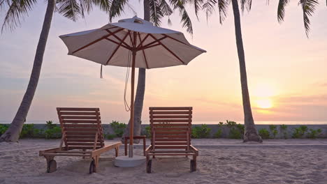 Tropische-Inselküste-Bei-Sonnenuntergang-Und-Zwei-Liegestühle-Unter-Einem-Sonnenschirm-In-Der-Nähe-Des-Strandes