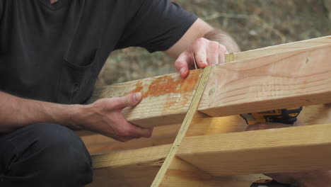 Closeup-of-Man's-Hands-Holding-Wooden-Plank-While-Person-Drills-Screw,-DIY-Homemade-Backyard-Skateboard-Ramp