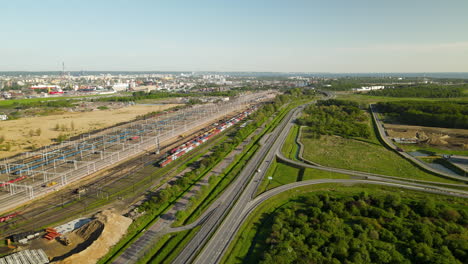 Large-Train-Depot-With-Many-Cargo-Trains-in-Terminal,-Gdansk-cityscape-on-background,-Poland,-sunny-weather-aerial-shot