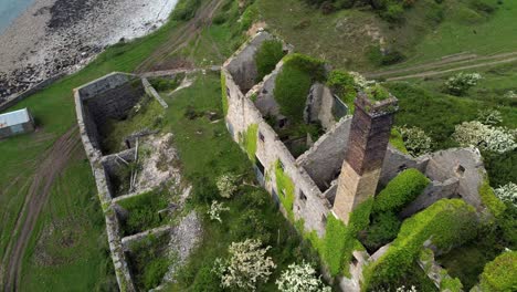Abandoned-overgrown-ivy-covered-desolate-countryside-historical-Welsh-coastal-brick-factory-mill-aerial-view-orbit-right-birdseye