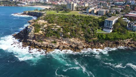 Waves-Crashing-On-Rocky-Cliff-Of-Peninsula-With-Waterfront-Hotels---Gordons-Bay-In-Coogee,-NSW,-Australia