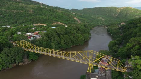 Drone-Aerial-View,-Yellow-Bridge-Above-Muddy-Magdalena-River-in-Green-Landscape-of-Colombian-HIghlands-Near-Honda-Town,-Tolima-Region,-Revealing-Shot