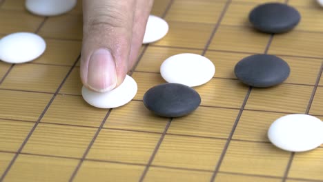 Close-up-on-Go-board-or-the-Chinese-chess-board-game,-fingers-holding-a-white-stone-to-attack-the-black-stone