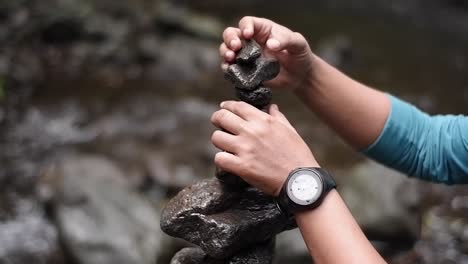 Eine-Nahaufnahme-Der-Hand-Eines-Mannes,-Der-Eine-Uhr-Trägt,-Die-Einen-Felsen-Auf-Einem-Fluss-Stapelt-Und-Balanciert