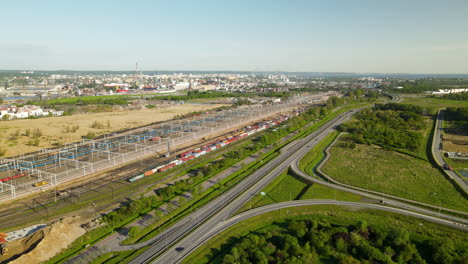 -Large-Train-Depot-With-Many-colorful-Cargo-Trains-next-to-the-Highway-Road-in-Gdansk,-Poland-aerial-view