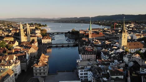 Aerial-flyover-over-Zurich,-Switzerland-above-Limamat-river-with-views-of-the-various-churches,-rooftops,-and-lake