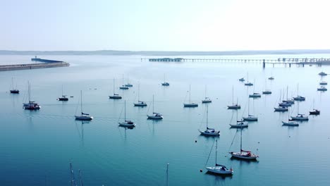 Sunny-Holyhead-harbour-breakwater-maritime-yachts-docked-along-transparent-calm-blue-shoreline-aerial-view