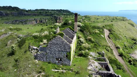 Abandoned-overgrown-ivy-covered-desolate-countryside-historical-Welsh-coastal-brick-factory-mill-aerial-view-orbit-left-to-rear