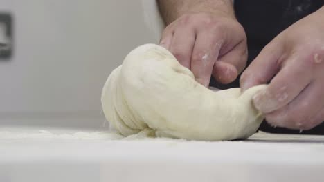 Slow-motion-close-up-of-a-baker's-hands-dropping-dough-onto-a-pile-of-flour-and-kneading-it