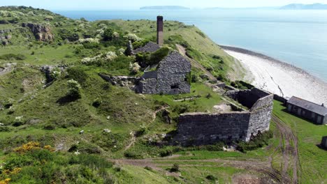 Abandoned-overgrown-ivy-covered-desolate-countryside-historical-Welsh-coastal-brick-factory-mill-aerial-view-rear-push-in