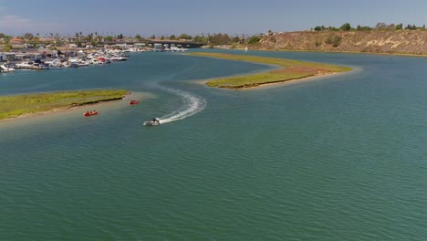 Aerial-view-of-a-small-boat-and-Kayakers-exploring-an-inlet-in-Newport-Beach,-California