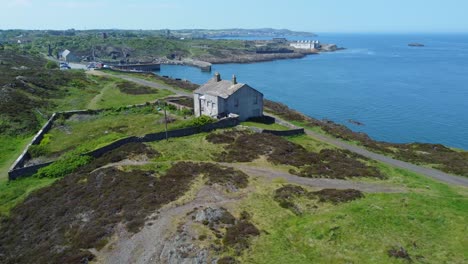 Abandoned-Amlwch-coastal-countryside-mountain-house-aerial-pull-away-view-overlooking-Anglesey-harbour