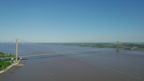 Aerial-wide-angle-pull-out-shot-showing-both-towers-of-the-Humber-suspension-bridge-spanning-the-river---professional-smooth-footage